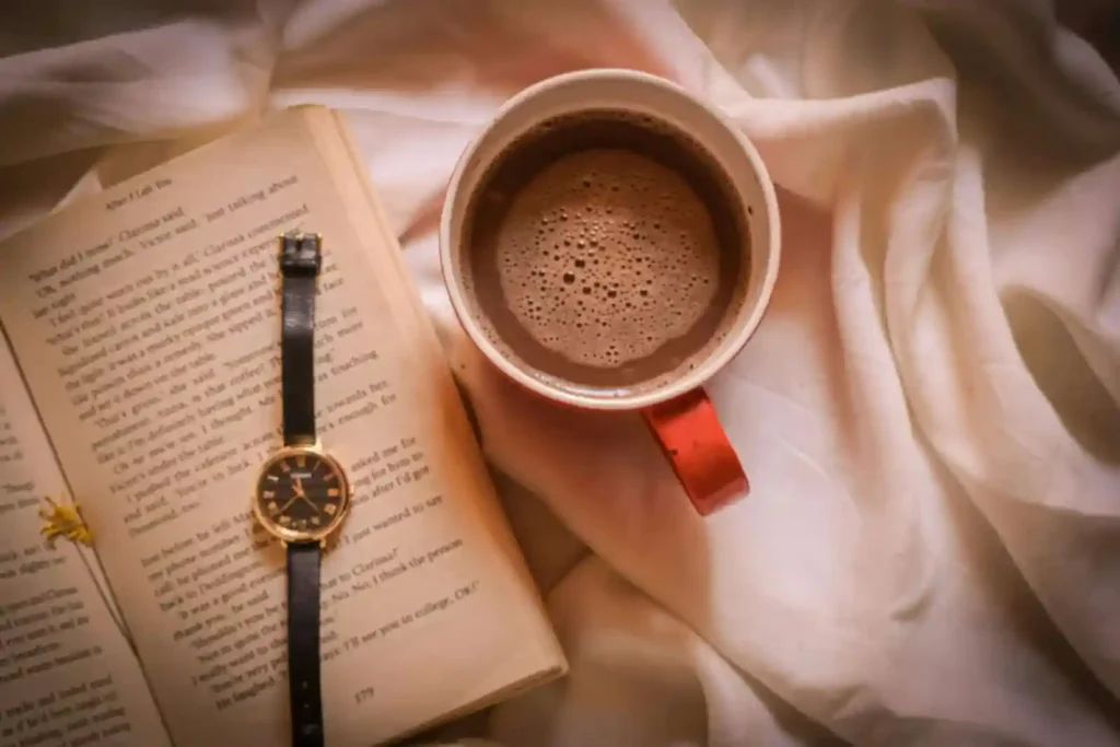 Cozy reading setup with open book, coffee cup, and watch on white bedding - perfect for overcoming reading slump